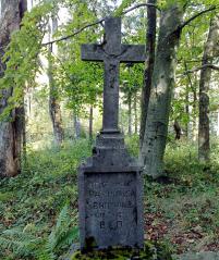 A stone tombstone in the form of a board with Russian inscriptions and a cross embedded on it. A tombstone in the midst of a deciduous forest.